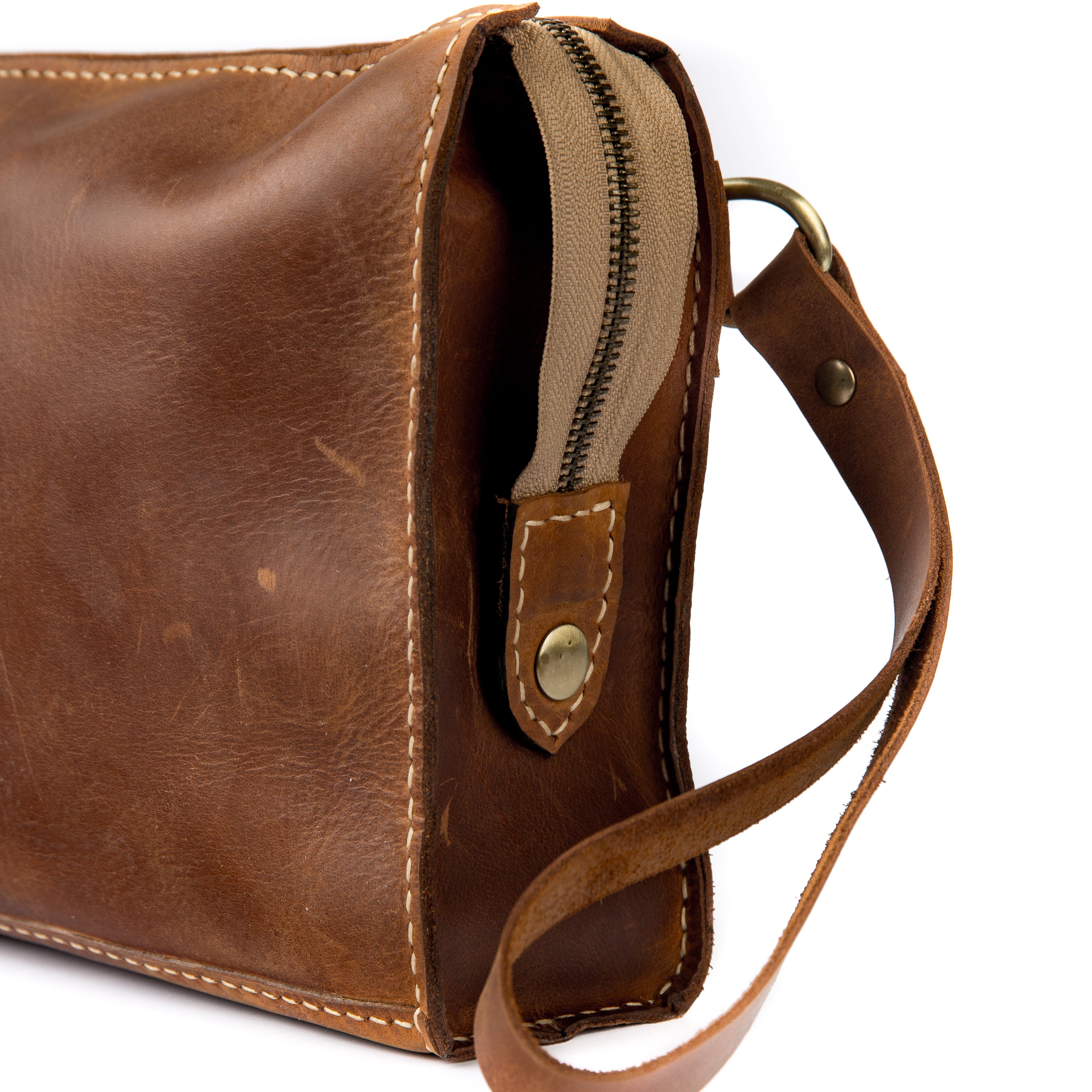 Handmade brown full-grain leather clutch with a brass zipper and side strap.