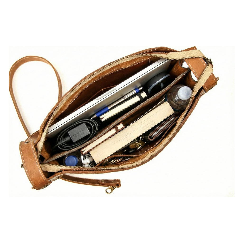 Comprehensive top-down view of the open interior of the tan leather 'Grand Braided Pack', filled with items including a laptop, notebooks, pens, charger, and a water bottle, highlighting the bag's large capacity and internal organization.