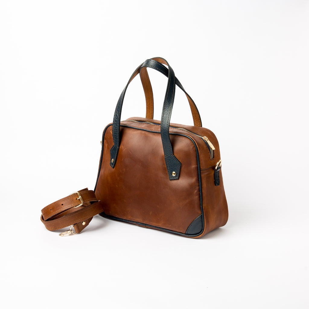 Lionell "Cairo Muse" leather handbag, side view, with the detachable brown leather shoulder strap coiled next to it.