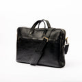 Front view of 'The Noir' pebbled leather laptop bag by LIONELL. Handcrafted from premium black textured leather, featuring a front zippered pocket, sturdy top handles, and a comfortable shoulder strap with a branded shoulder pad, displayed on a clean white background.