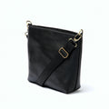 A side-view photo of 'The Urban Crossbag' by LIONELL; handcrafted from rich black genuine leather, featuring a modern slim design with visible stitching and an adjustable black fabric shoulder strap, displayed on a clean white background.