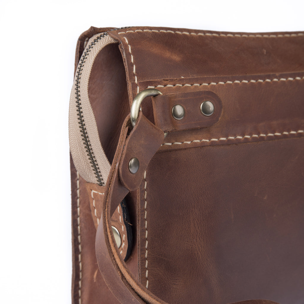 Close-up of a brown full-grain leather clutch featuring white stitching and brass hardware.